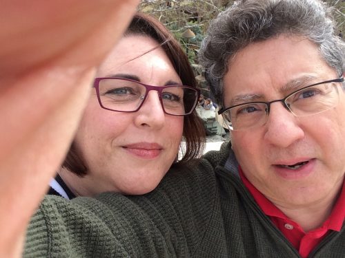 The author, Pia, peering over her boyfriend's right shoulder. Pia is wearing glasses. Her boyfriend is also wearing glasses, a green sweater with the red collar of his shirt showing at the top