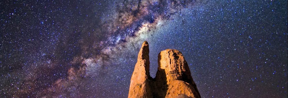 Photo of a brownish rock structure against the milky way