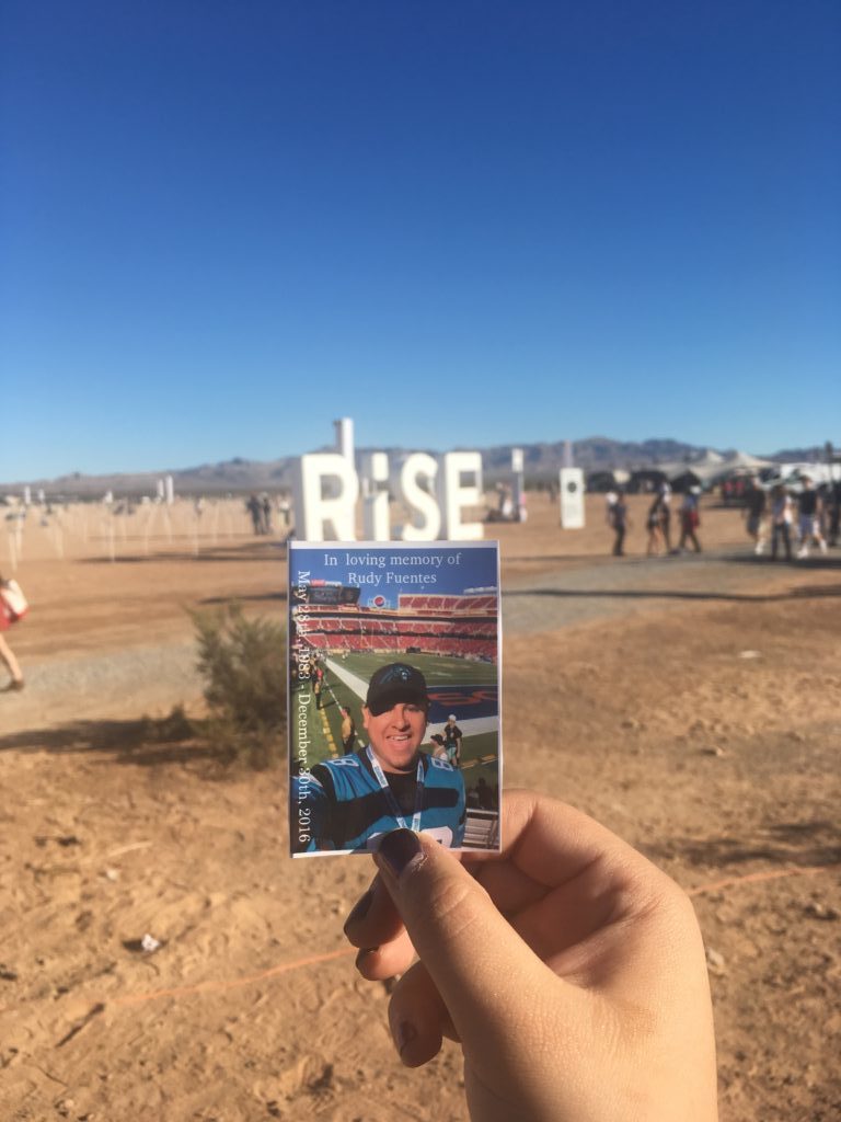 Alyssa holding a photo of Rudy with the caption at the top that says "In loving memory of Rudy Fuentes". The word RISE can be seen in the background.