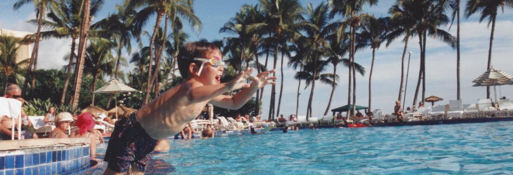 Jimmy age four jumping into a pool at the Hyatt Maui. He's wearing blue swim trucks and goggles