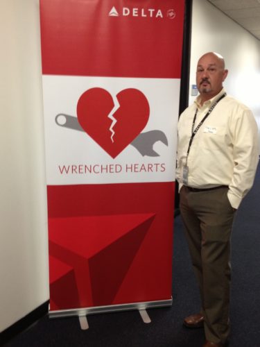 Tim Moye, the author, staying next to a red banner with the words Wrenched Heart and the Wrenched Hearts logo on a white background