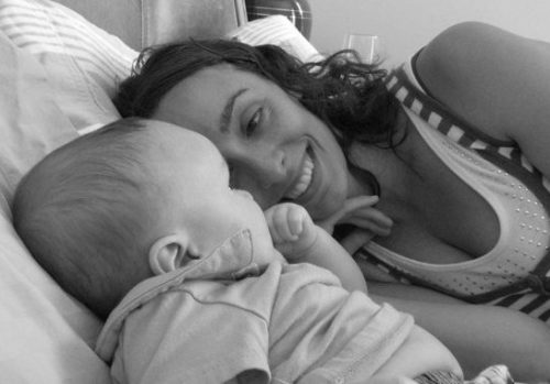 Black and white photo of Erin Benson laying on her left side smiling and gazing at her baby Sam.
