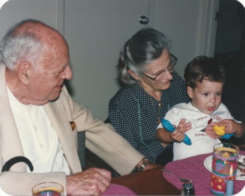 Dad in a beige sport coat and white color shirt sitting next to Mom who's wearing a black print blouse and glasses holding Jimmy age 2