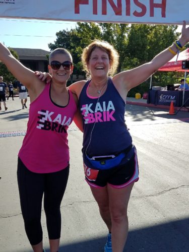 Coach Natalie on the right wearing sunglasses and a pink Kaia BRIK tank top and black leggings. Margo on the right wearing navy tank with Kaia BRIK on it and black shorts with pink piping.