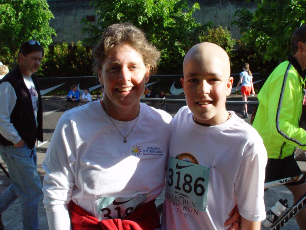 Margo and Jimmy after a race in 2006. Margo is on the right wearing a long sleeve white t-shirt that says "Portland Children's Museum". Jimmy is on the right, bald from cancer treatment wearing a short sleeve white t-shirt with the number 3186 pinned to the front