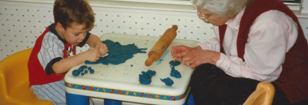 Jimmy and Barbara playing with blue PlayDoh. They're sitting at a little table with blue legs and yellow chairs.