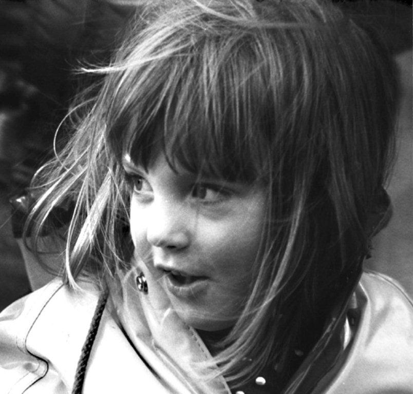 Alexandra age 5 looking to her right (our left). She's wearing a light colored coat. Her hair is shoulder length and is being blown by the wind. The photo is black and white.