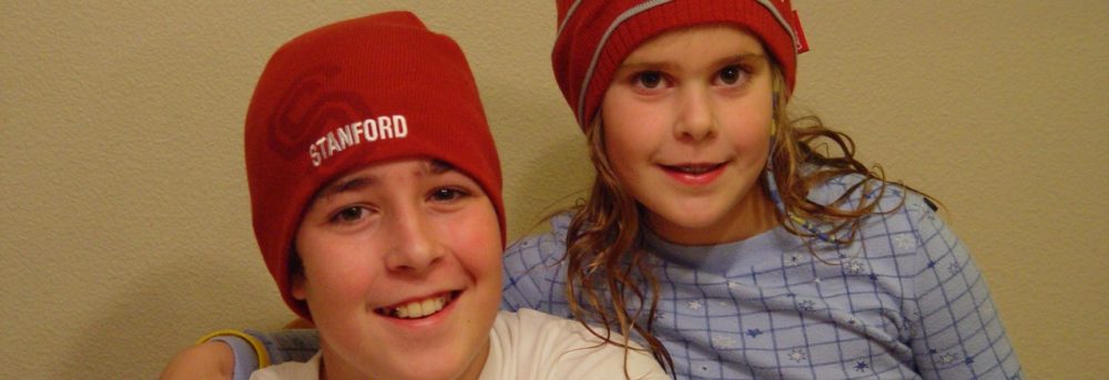 Jimmy and Molly wearing dark red Stanford skull caps. Jimmy is on the left wearing a white short-sleeve t-shirt. Molly is wearing light blue checked PJs