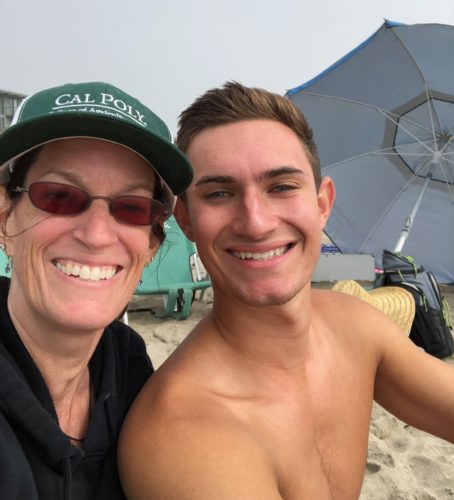 Julie and Brenden. Julie is wearing a black collared shirt with a green CalPoly hat and sunglasses. Brenden is shirtless with his brown hair slicked back