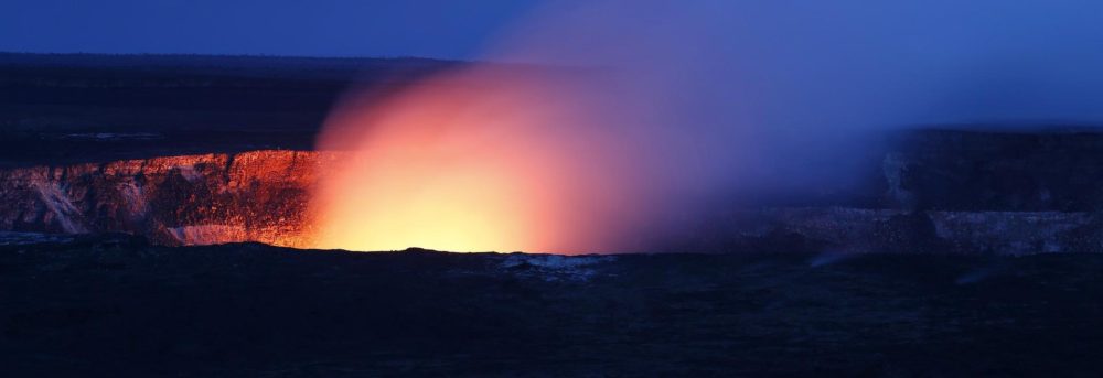 Red and yellow glow of a volcano against a dark blue sky