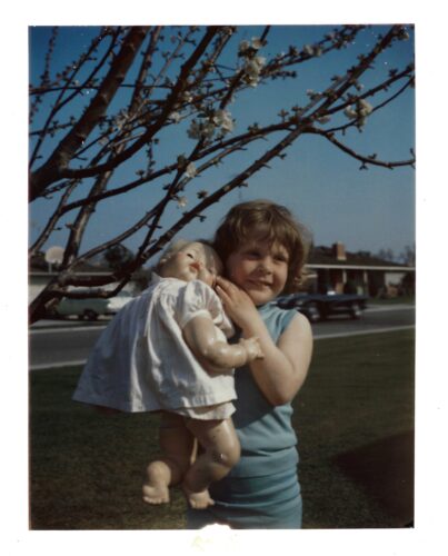 Margo standing under the cherry tree at age 4 holding a bald baby doll